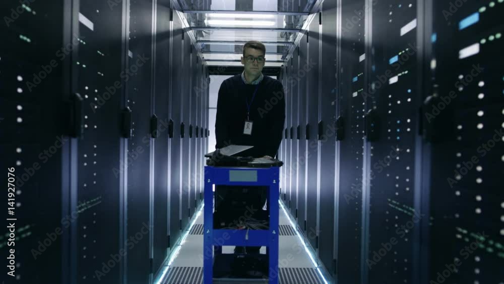 Poster it engineer pushes crash cart in the data center corridor with rows of rack servers. shot on red epi