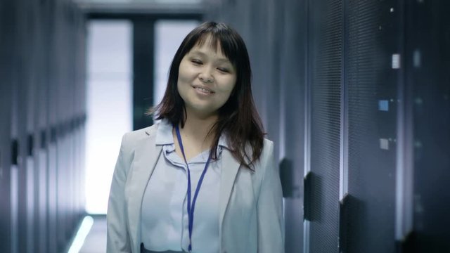 Close-up of Female Asian IT Engineer Smiling while Standing in Data Center full of Rack Servers. Shot on RED EPIC-W 8K Helium Cinema Camera.