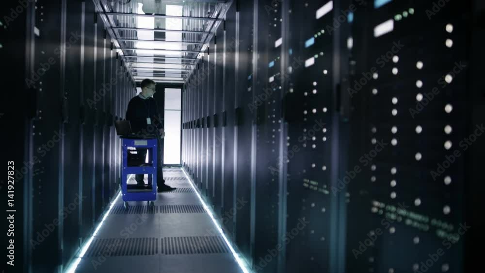 Poster it engineer pushes crash cart in the data center corridor with rows of rack servers. he opens rack s