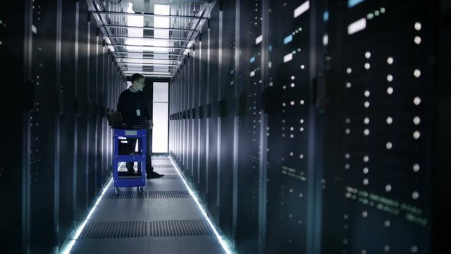 IT Engineer Pushes Crash Cart in the Data Center Corridor with Rows of Rack Servers. He Opens Rack Server Cabinet. Shot on RED EPIC-W 8K Helium Cinema Camera.
