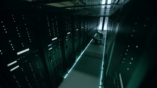 Security Camera Footage of Hacker in a Hoodie Inflitrating Data Center, With His Laptop He Connects to One of The Rack Servers. Shot on RED EPIC-W 8K Helium Cinema Camera.