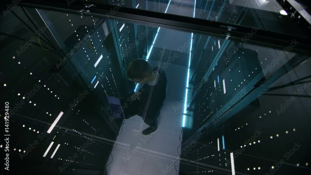 Poster top view through the glass of it engineer working with laptop in data center full of active rack ser