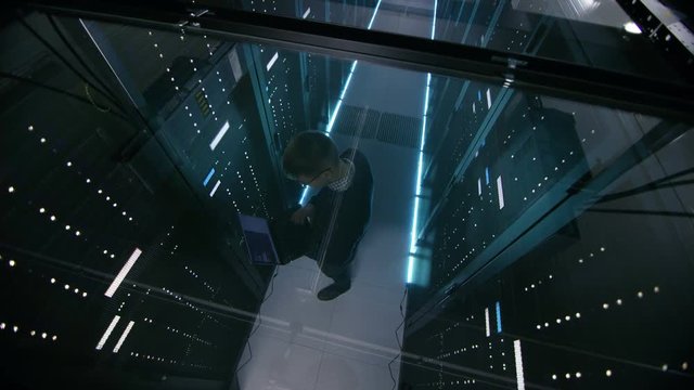 Top View Through the Glass of IT Engineer Working with Laptop in Data Center Full of  Active Rack Servers. Shot on RED EPIC-W 8K Helium Cinema Camera.