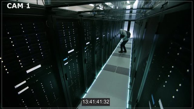 Security Camera N1 Footage of a Hooded Hacker in Data Center, With His Laptop He Connects to One of The Rack Servers, Commits Crime and Leaves. Shot on RED EPIC-W 8K Helium Cinema Camera.