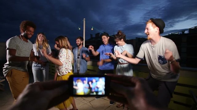 View Of Hands Holding Phone And Filming Multi-ethnic Couple Dancing In The Middle And Friends Dancing Around Them