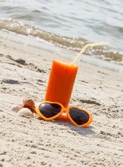 Carrot juice and sunglasses at beach, concept of vitamin A and beautiful, lasting tan