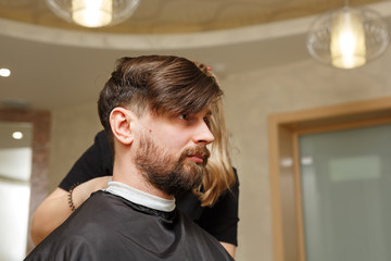 Professional hairdresser doing haircut men's hair. Cutting electric razor. Beauty saloon. Male beauty. The client is a hipster.