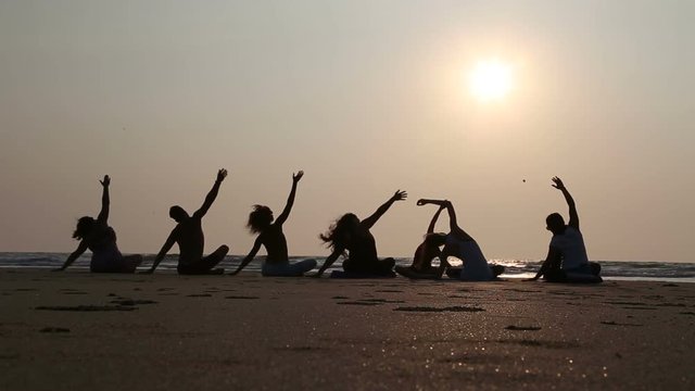 People practicing yoga at a sandy beach in Goa at sunset.