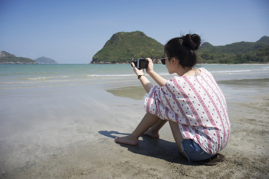 Asian teenager woman has take a relaxing on beautiful beach. Wearing sunglasses and holding a camera. Siam Smiling girl. rest time at the beach with big mountain. Filtered image. Selective focus