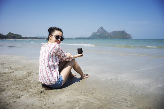Asian teenager woman has take a relaxing on beautiful beach. Wearing sunglasses and holding a camera. Siam Smiling girl. rest time at the beach with big mountain. Filtered image. Selective focus