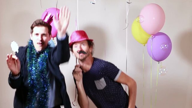 Two smiling happy men dancing with props in photo booth