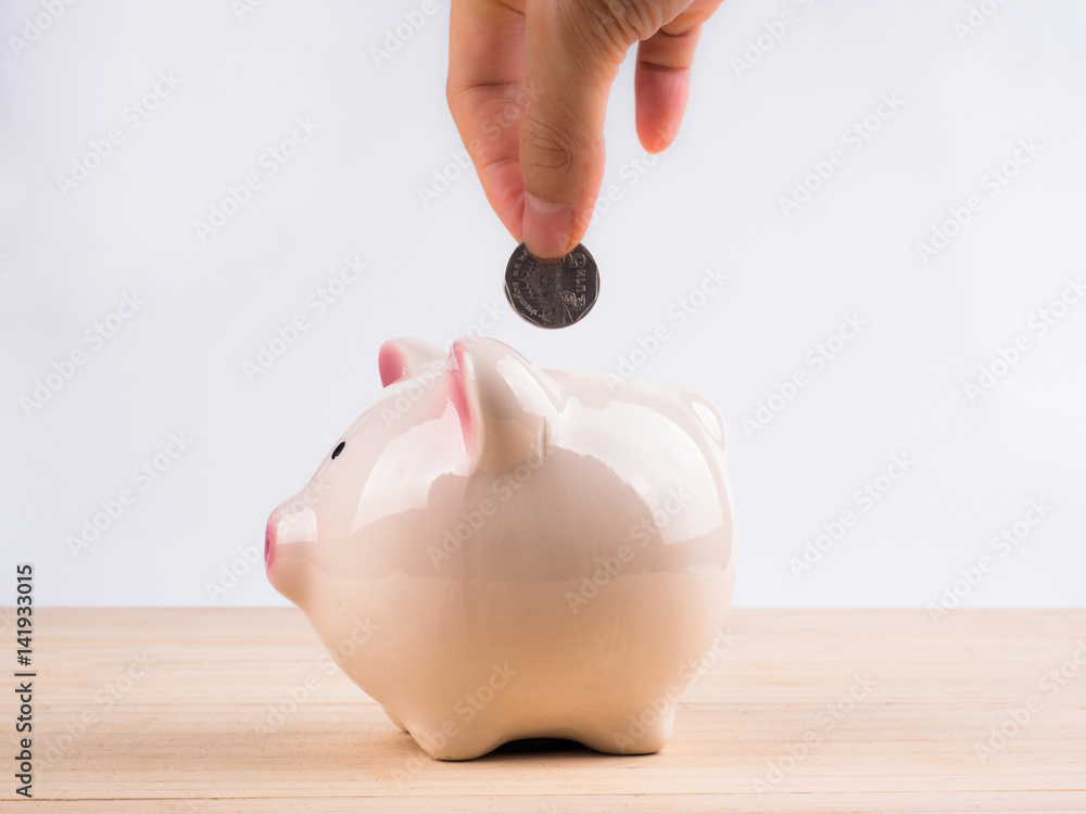 Wall mural hand putting a coin into a pink piggy bank in saving money for future concept