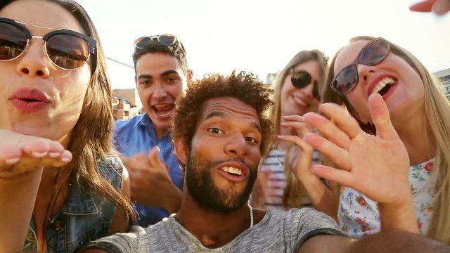 Close up of happy crazy multi-ethnic group of friends filming themselves at rooftop party on sunny day, graded