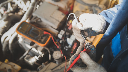 Mechanic in auto workshop works with car electrics - electrical wiring, voltmeter - top view