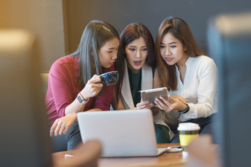 3 woman using tablet and laptop in coffee shop, surprise and exiting on what they see on the screen