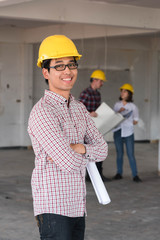 Asian Construction engineer smile wear yellow safety helmet with blue print of construction plan and tablet in hand