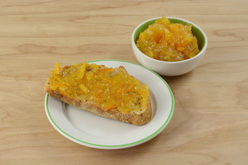 Orange marmalade in condiment bowl and on piece of wholegrain toast