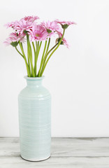 Pink gerbera flowers in blue ceramic vase, white background