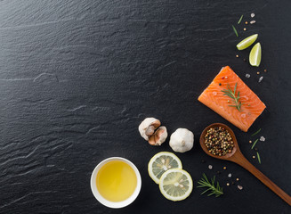 Beautiful composition of fresh salmon fillet with rosemary, salt, oil, lemon and peppercorn on dark background. Good for space and background