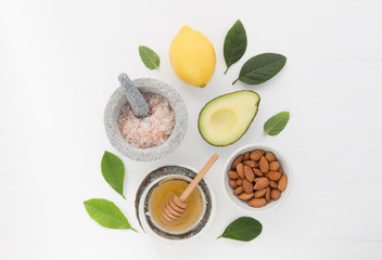 Homemade skincare and body scrubs with natural ingredients almond, avocado, lemon, himalayan salt, peppermint leaves and honey set up on white wooden background