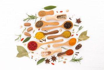 Various herbs and spices on wooden spoons. thyme, cinnamon, anise, nutmeg, rosemary, peppercorn, salt, paprika, turmeric, chilli, nutmeg, oregano, and cardamom on wooden background