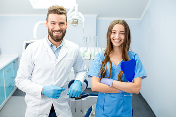 Portrait of handsome dentist with young female assistant in uniform at the dental office