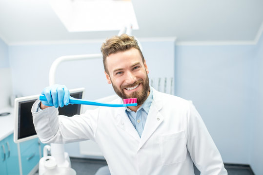Portrait of funny dentist in uniform with big toothbrush at the dental office