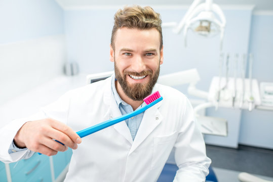 Portrait of funny dentist in uniform with big toothbrush at the dental office
