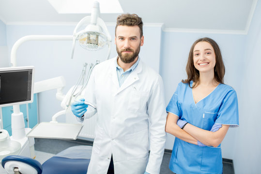 Portrait of handsome dentist with young female assistant in uniform at the dental office