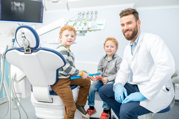Portrait of handsome dentist and happy boys sitting on the chair at the dental office