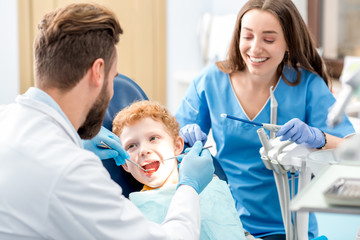 Children's dentist and assistant examinating baby teeth of a young boy sitting on the dental chair...
