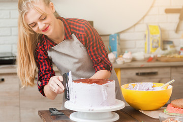 Young cute woman making biscuit cake with white cream on wooden kitchen table. Culinary masterclass of cooking desserts. Blogger preparing colorful festive food