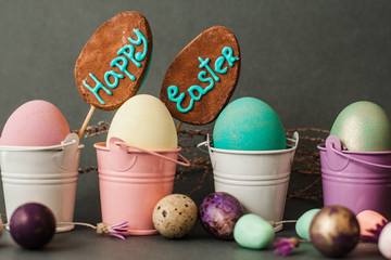 Four painted easter eggs in color buckets with two cake-pops on grey background closeup. Easter greeting card