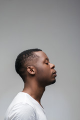 Concentrated african guy with closed eyes on grey background with free space. Getting new ideas,...