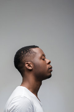 Concentrated african guy with closed eyes on grey background with free space. Getting new ideas, deep concentration, yoga, meditation. Profile view.