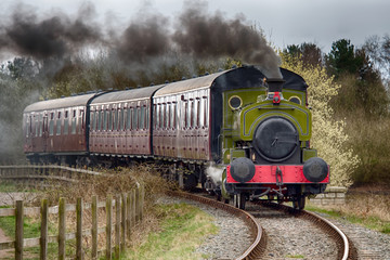 A steam train locomotive traveling forward with smoke emerging from the funnel.