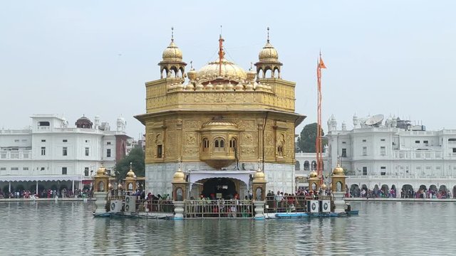 Golden temple in Amritsar, with water in front and crowd standing by entrance.