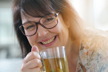 Smiling mature woman with eyeglasses drinking infusion
