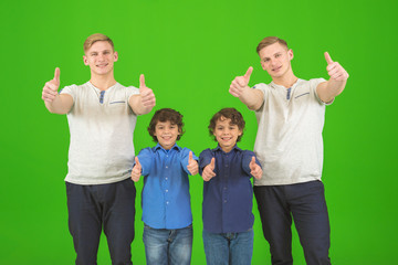 The four cute brothers stand on the green background and thumb up