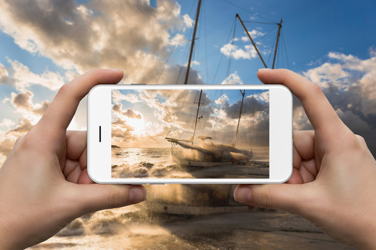 Female hands with a smartphone close-up. Photographing a ship and a storm in the sea at sunset