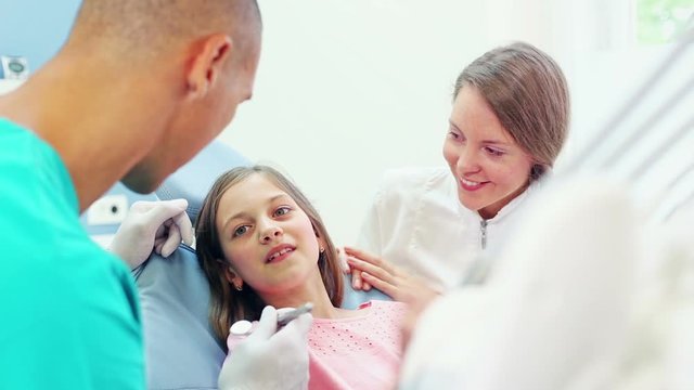 Close up of cute little girl in dental chair shows with finger aching tooth, dentist and assistant examining the girl, graded