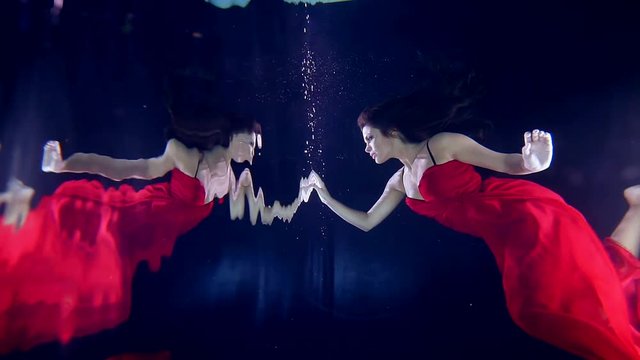 girl is floating under the water and touches her reflection as mirrors