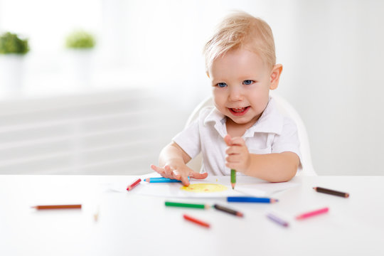 Happy baby boy draws with colored pencils.