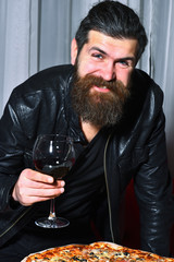 Happy bearded man toasting glass of red wine over pizza