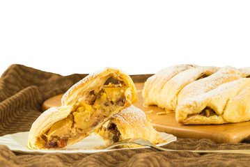 Close up of a slice of homemade apple strudel (apples pie) with puff pastry, cinnamon and raisin, on a white background    
