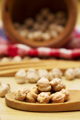 Wooden bowl with chickpeas and spoon on wooden table with red tablecloth