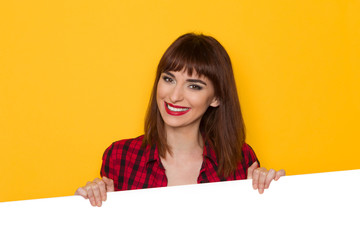 Fototapeta premium Smiling Girl In Red Lumberjack Shirt Behind White Banner