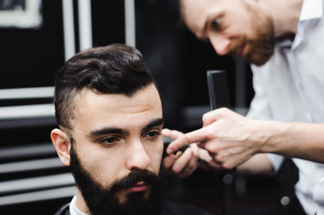 Master cuts hair and beard of men in the barbershop, hairdresser makes hairstyle for a young man