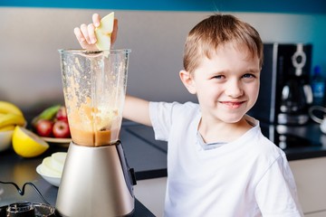 Little child boy adding piece of melon to blender