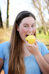 Young happy woman is standing in park and eating apple.